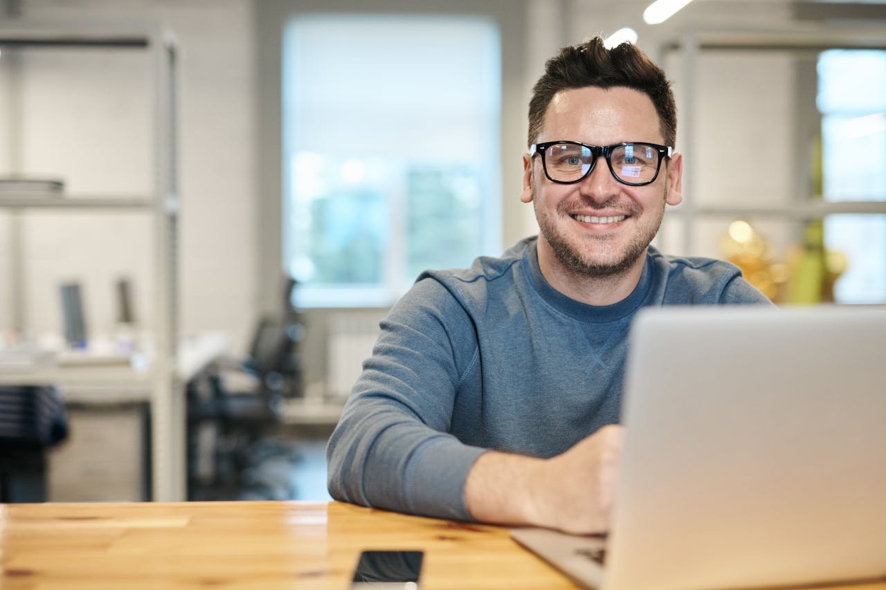 gallery-6 Happy man wearing glasses working remotely on laptop in modern office environment.
