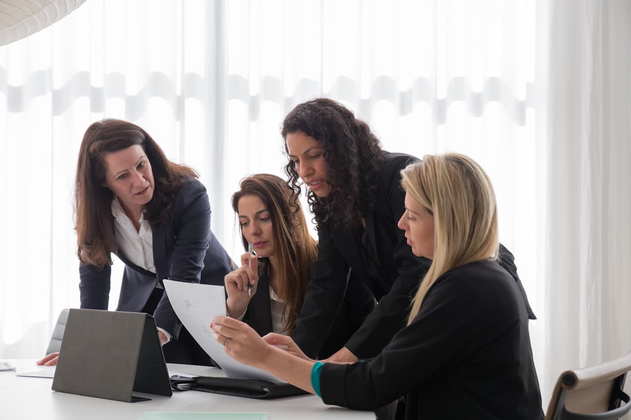 our-services-3 Four businesswomen engaged in discussion over documents in a contemporary office setting.